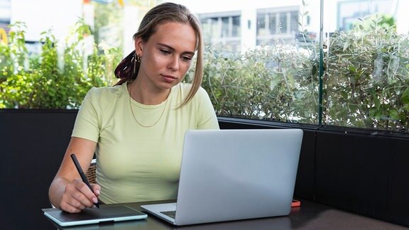 Eine Frau im gelben Shirt sitzt von einem Laptop und lernt