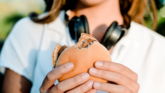 Close-up von einer Frau, die einen Hamburger in der Hand hält