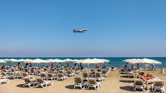 Touristen am Strand beobachten die Landung eines Passagierflugzeugs an einem heissen Sommertag
