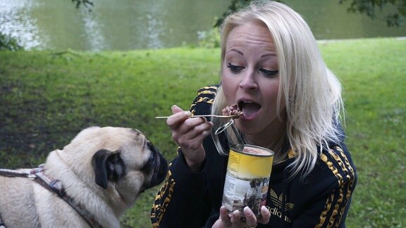 Eine Frau isst Hundefutter aus der Dose, während ihr Hund zusieht