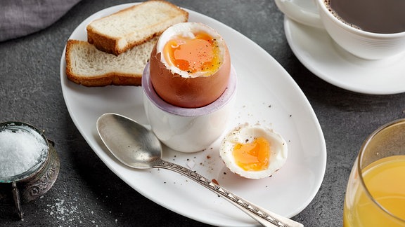 Auf einem Frühstückstisch ist ein geköpftes Ei mit Löffel