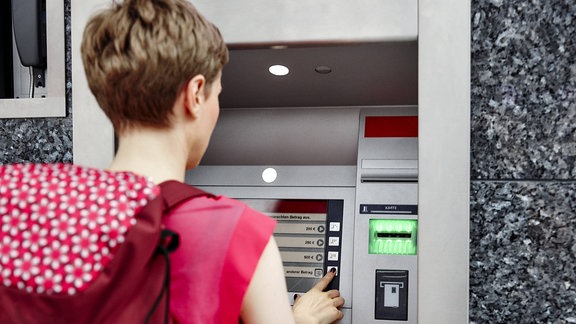Eine Frau hebt an einem Bankautomaten Geld ab