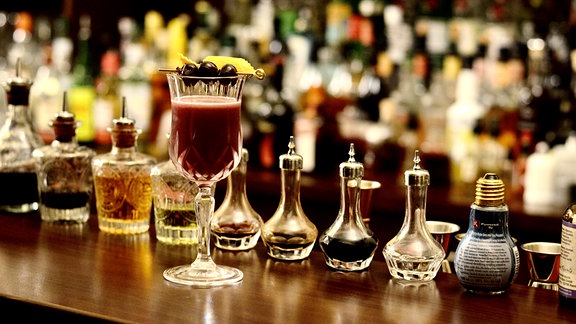 Ein Glas gefüllt mit Glühwein auf dem Tresen einer Bar. Dekoriert mit 3 schwarzen Beeren.
