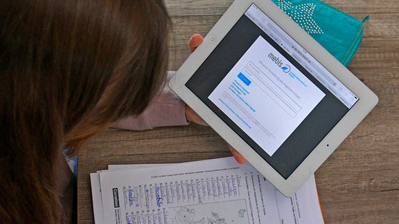 Mädchen sitzt am Schreibtisch und lernt ihre Unterrichts-Aufgaben auf dem iPad.