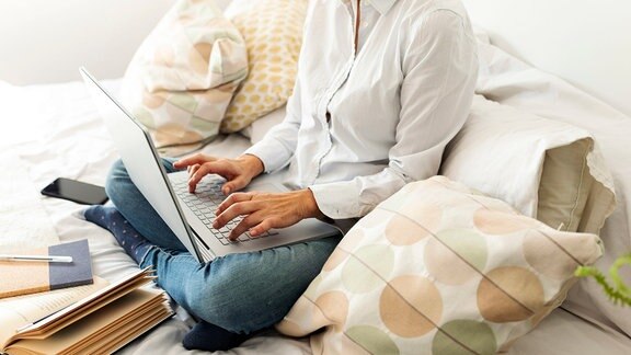 Eine Frau sitzt auf dem Bett und arbeitet am Laptop