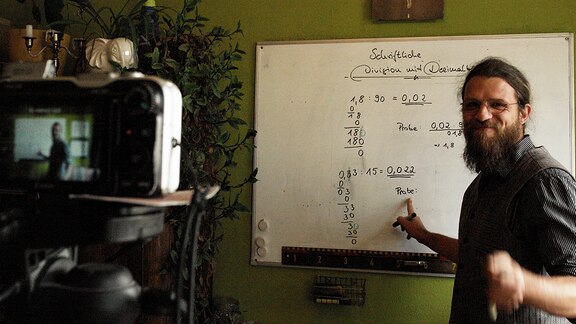 Lehrer Jakob Meier in seinem Arbeitszimmer vor einer Tafel.