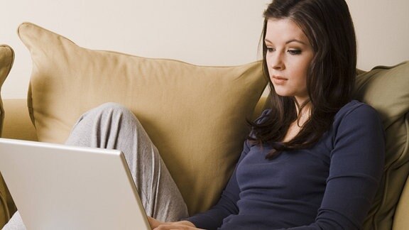 Junge Frau im Homeoffice am Laptop auf der Couch