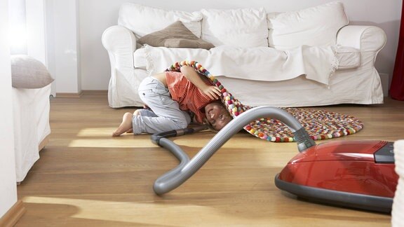 Junge saugt im Wohnzimmer auch unter dem Teppich vor dem Sofa (Symbolbild)