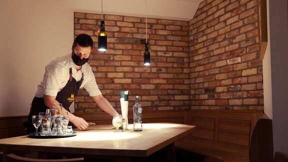 Ein Kellner mit Mundschutz räumt einen Tisch in einem Restaurant ab