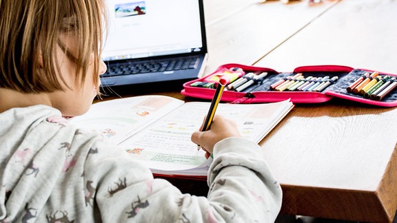 Schulkind sitzt am Tisch vor Laptop und löst Aufgaben aus dem Homeschooling