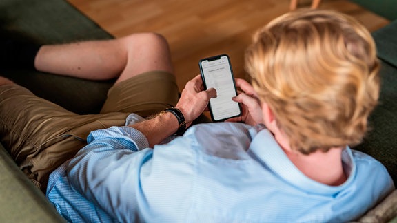 Ein Mann liest auf dem Smartphone eine Nachricht (Symbolbild)  