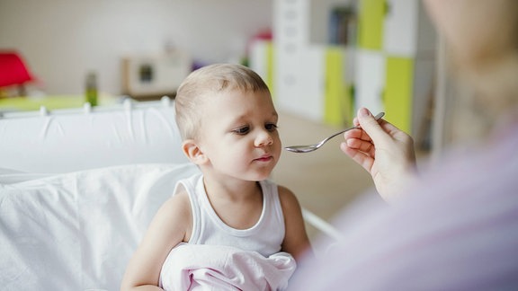 Einem Kind wird Medizin auf einem Löffel gereicht