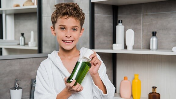 Ein Junge im Bademantel hält eine Flasche Mundspülung in der Hand.