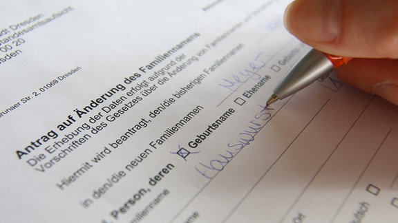 Eine Frau füllt mit einem Kugelschreiber der Antrag auf Änderung des Familiennamens aus