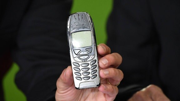 Eine männliche Hand hält ein altes Nokia Handy aus den 90ern in die Kamera. 