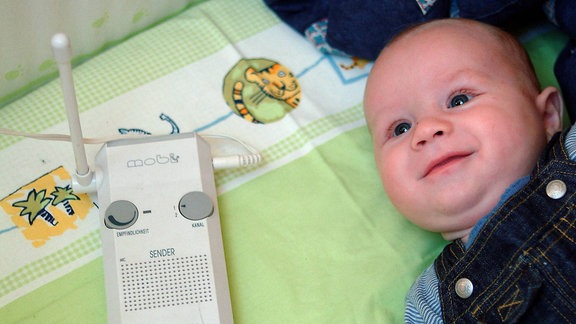 Lachendes Baby mit einem Babyphone daneben