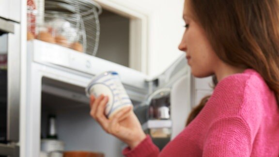 Frau wirft Lebenmittel aus dem Kühlschrank in den Müll