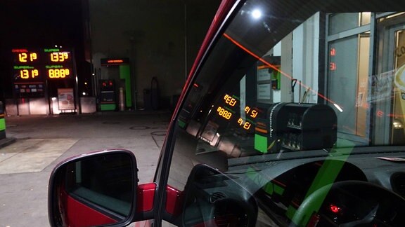 An einer Tankstelle spiegeln sich die Spritpreise in einem Autofenster