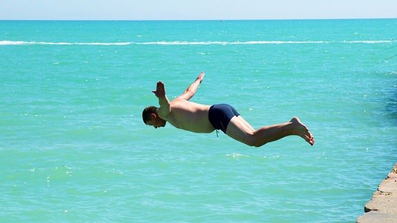Ein Mann in Badehose springt ins Meer.