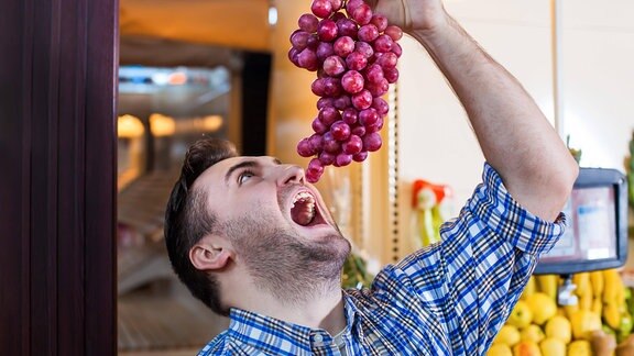 Mann versucht im Supermarkt eine Weintraube zu essen
